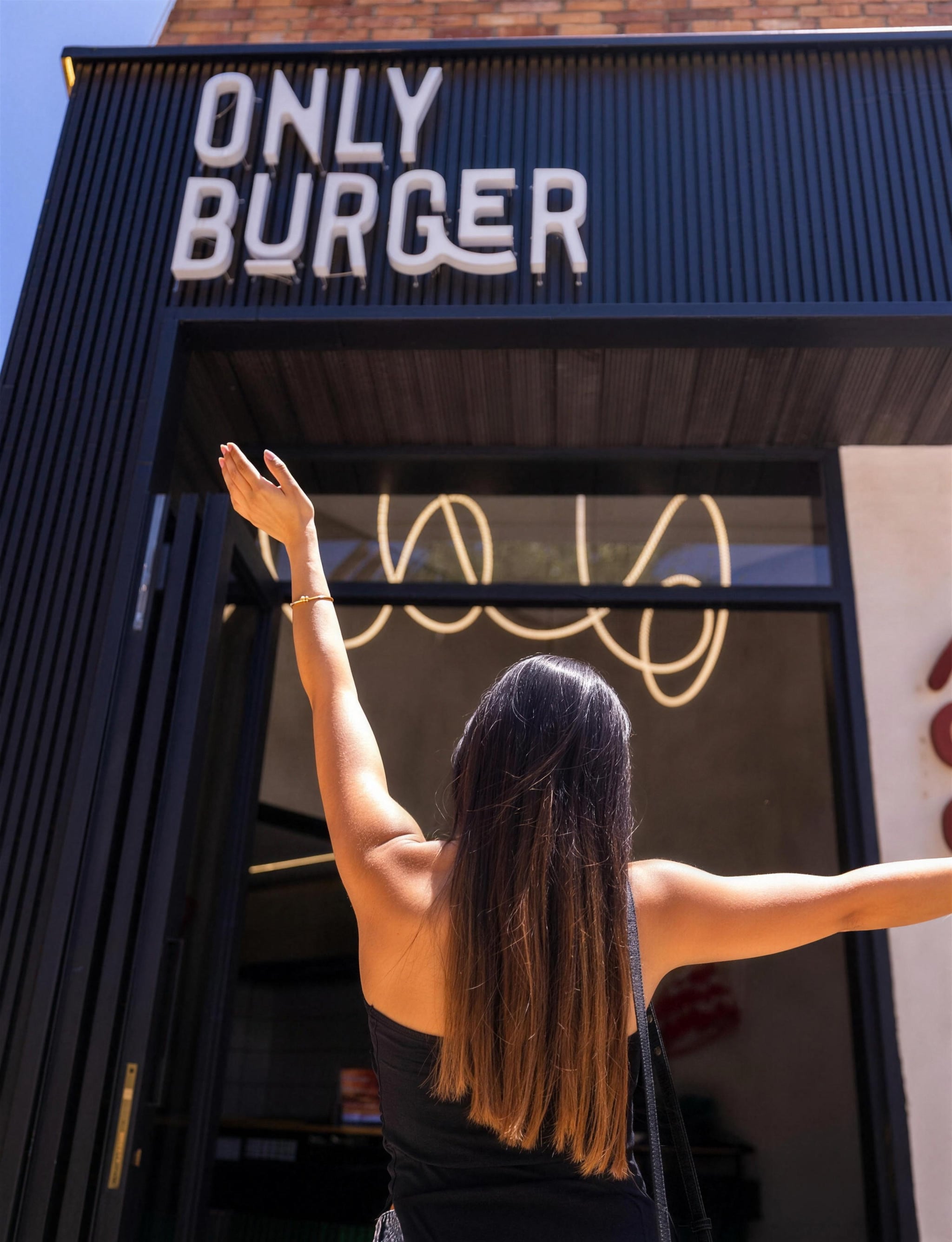 A guest with her arms raised outside OB Only Burger at Rayfoun Square