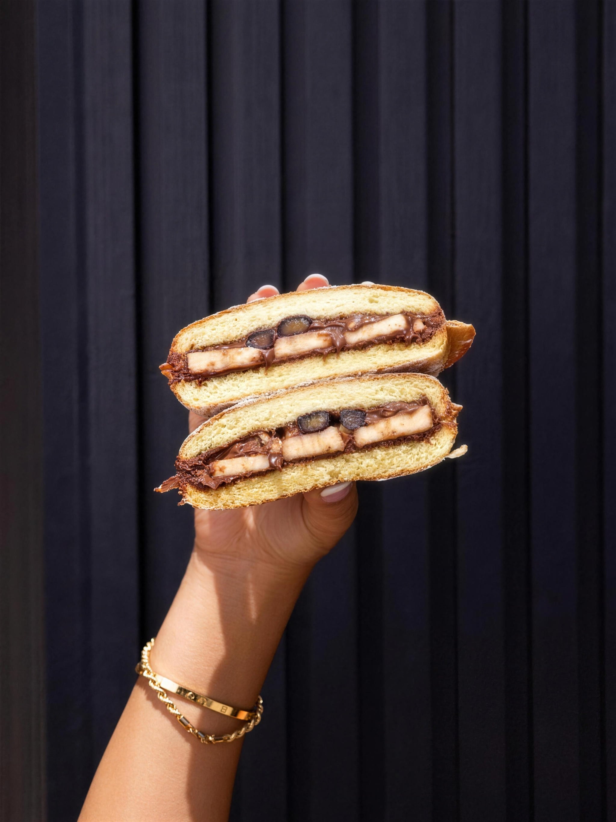 A brioche filled with chocolate spread and banana, held up against a dark wall