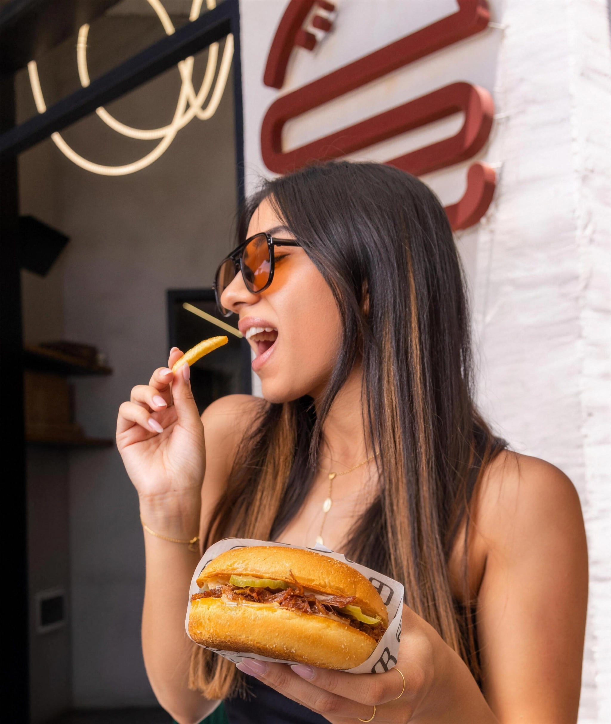 A guest eating fries with a burger in hand outside OB Only Burger