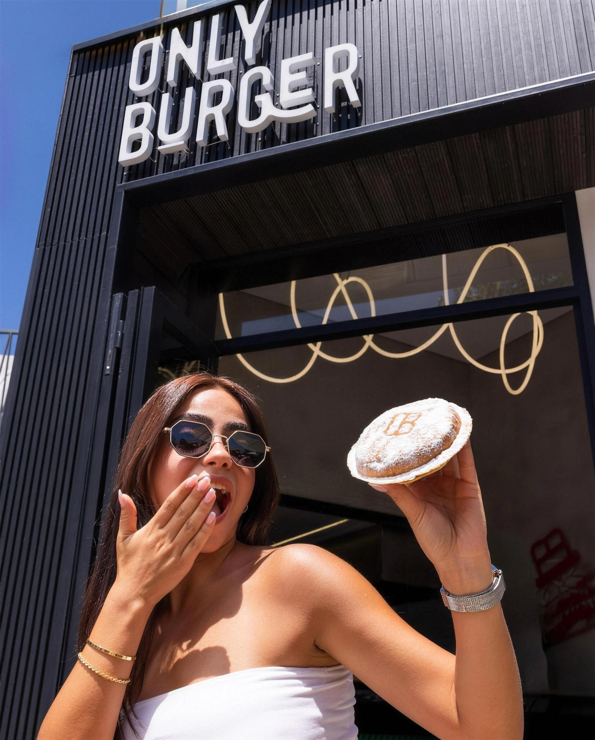 A guest holding a sugar dusted pastry outside OB Only Burger